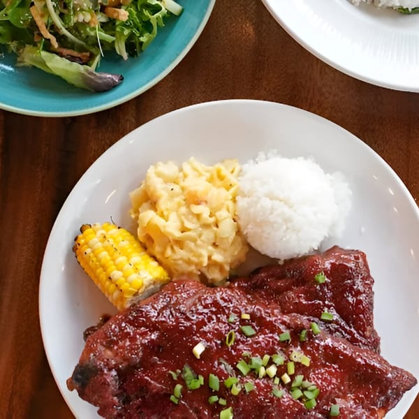 Plate of BBQ ribs with mashed potatoes, corn on the cob, and white rice, with a side salad.